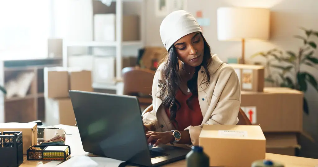 Small business owner preparing online orders beside a laptop in an ecommerce workspace